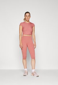 Top d'athlétisme rose court et leggings taille haute, tous deux en tissu extensible. Le modèle porte des baskets roses claires et des chaussettes blanches.