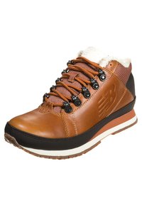 Brown leather mid-top sneaker with a textured fabric collar, black accents, circular lacing, and a white sole. Features a fuzzy lining.