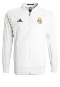 Witte sportieve jack met volledige rits, ribgebreide manchetten en zoom, Adidas-logo in marineblauw, Real Madrid-embleem op de linkerborst, gladde stoftextuur.