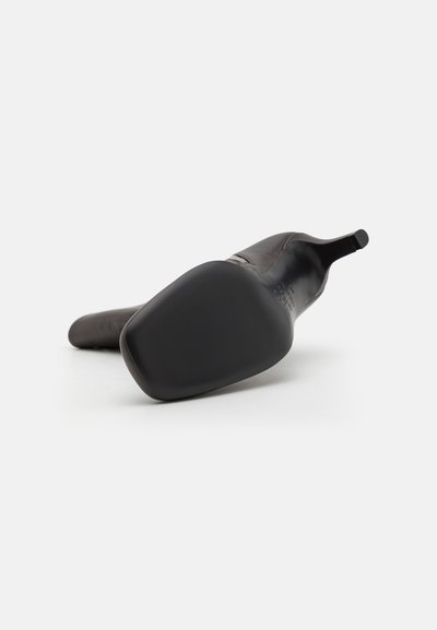 Svart högklackad sko visad från underifrån, med en slät yta, spetsig tå och en smal klack. Sulan är platt och rundad.