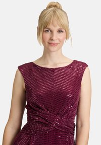 Robe bordeaux profond avec un corsage ajusté, des manches courtes et un motif texturé agrémenté de sequins pour un effet scintillant.
