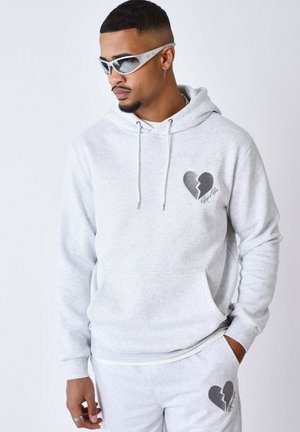 Sudadera con capucha gris, con un bolsillo central y un gráfico de un corazón roto. Tejido texturizado, con prendas inferiores grises a juego.