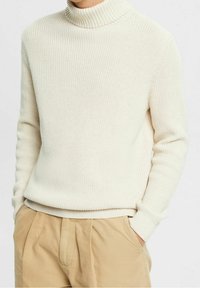 Cremefarbener, gerippter Rollkragenpullover aus strukturiertem Strickmaterial, mit einer taillierten Passform und leicht umgeschlagenem Kragen.