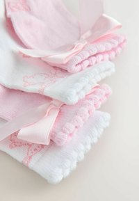 Pile de chaussettes pour bébé roses et blanches pliées, présentant des bords festonnés et de petits nœuds en satin sur un fond clair.