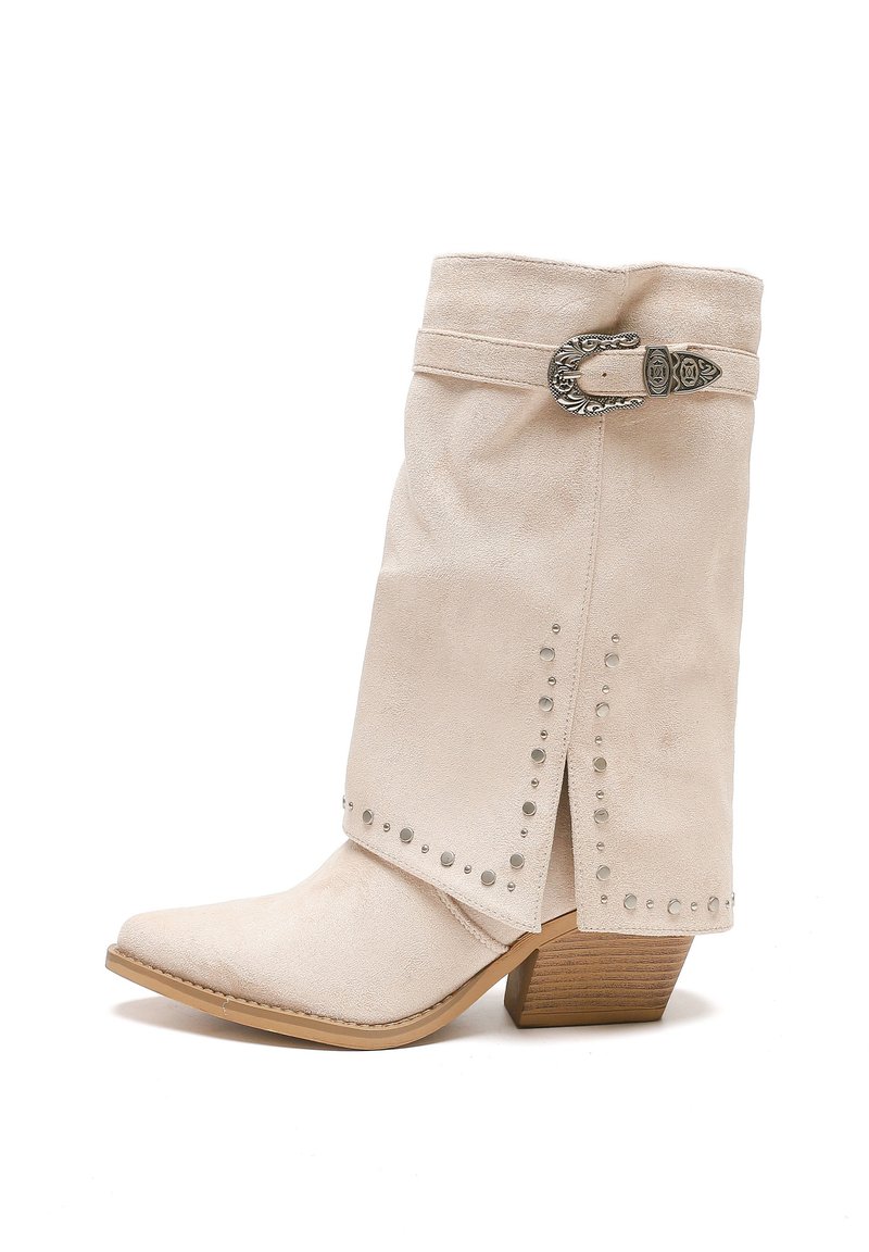 Botín de gamuza beige con punta afilada, acentos con tachuelas plateadas, una hebilla decorativa y un tacón de madera apilada.