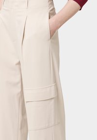 Beige cargobroek met zijzakken, geplisseerd ontwerp en een gladde textuur. Voorzien van een klepzak op de dij.