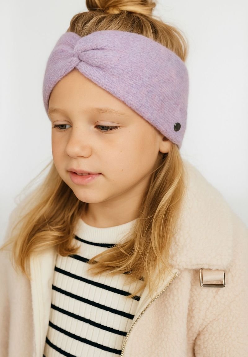 Ragazzina con capelli biondi raccolti in un chignon, che indossa una fascia di lana lavanda, un maglione a righe e una giacca morbida di colore crema.