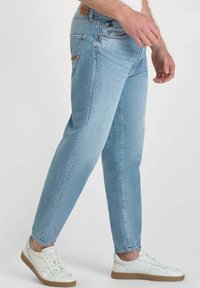 Jeans in denim blu chiaro con una vestibilità affusolata, caratterizzati da cuciture a contrasto e una tasca posteriore. Abbinati a scarpe bianche e una maglietta bianca semplice.