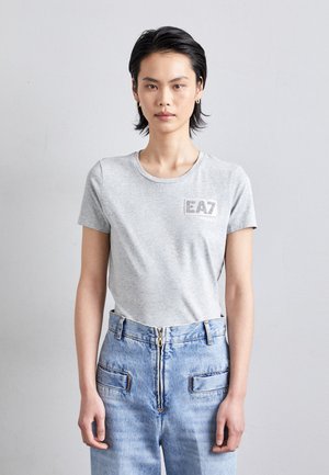Grijze crewneck t-shirt van katoen, met een logo op de voorkant in contrasterende kleur. Gecombineerd met lichtblauwe hoogwaistjeans.