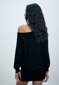 Čierne off-shoulder šaty z mäkkej pleteniny. Obsahujú dlhé rukávy, žebrované manžety a priliehavý strih na spodnej časti.