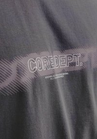 Grijze katoenen t-shirt met een gestructureerde, vervaagde graphic van "COREDEPT." in het wit, met aanvullend kleinere tekst in het wit aan de onderkant.