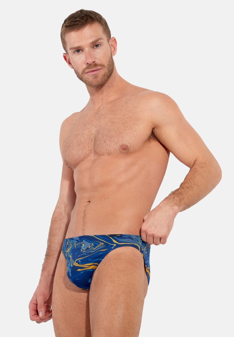 Marmorierte Schwimmslips in Blau, Gelb und Grün. Hergestellt aus glattem Stoff mit einem tiefen Schnitt, minimaler Hardware und einem komfortablen Bund.