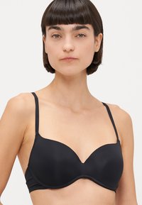 Reggiseno nero con ferretti e coppe modellate e senza cuciture, dotato di spalline sottili e regolabili, caratterizzato da una texture liscia e un design minimalista.