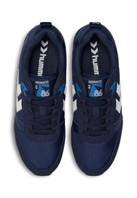 Mörkblå sportskor med vita och blå detaljer. Texturerad tygöverdel, snörningsdesign och förstärkt tåparti. "Monaco 86" märkt på tungan.