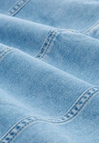 Lichtblau denimstof met een gladde textuur en zichtbare stiksels. De stof heeft een licht geborstelde afwerking, wat de zachtheid vergroot.