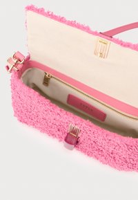 Ροζ τσάντα χειρός με υφή, που διαθέτει απαλό, αφράτο εξωτερικό και λείο δέρμα περιμετρικά. Η εσωτερική πλευρά έχει ανοιχτόχρωμη υφασμάτινη επένδυση με τσεπάκι με φερμουάρ.