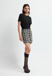 Top negro de manga corta combinado con una falda a rayas en blanco y negro. La modelo lleva medias altas negras y tacones abiertos.