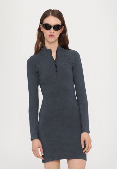 Rochie cu mâneci lungi, ajustată, de culoare gri închis, cu un fermoar pe jumătate în față și un material fin, texturat. Accentele includ un branding minimalist.