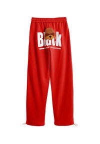 Pantalones de chándal rojos con cintura elástica, que presentan un diseño de perro marrón de peluche y un texto blanco bold "Black" en la pierna izquierda.