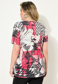 Top de manga corta con un patrón geométrico en negro, rojo y blanco, que presenta rostros abstractos y diseños en zigzag, hecho de una tela suave.