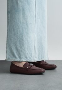 Brune læderloafers med en rundet tå og en dekorativ rem, kombineret med lyseblå vide bukser i denim. Teksturerede gummisåler.