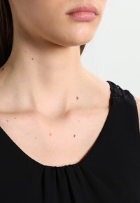 Czarna bezrękawnikowa odzież z okrągłym dekoltem, z koronkowymi detalami na ramiączkach i miękkim, teksturowanym materiałem.