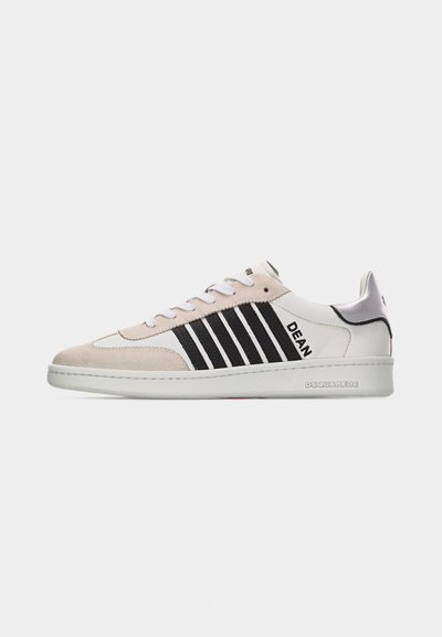 Baskets blanches et beiges avec des rayures noires, texte "DEAN" sur le côté, et "DSQUARED2" embossé sur la semelle blanche sur fond uni.