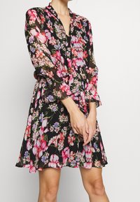 Sukienka w kwiaty na czarnym tle, z intensywnymi różowymi i fioletowymi kwiatami, długimi rękawami, dekoltem w kształcie litery V oraz elastyczną talią.