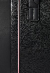 Black leather bag featuring a textured surface, with a smooth accent panel and a narrow red and white stripe detail. Structured design.