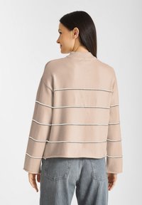 Lichtbeige trui met horizontale witte en zilveren strepen, ronde hals en zachte textuur, gecombineerd met grijze high-waisted jeans.