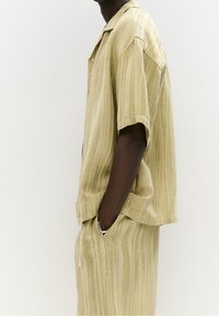 Korte mouwen, licht olijfgroene button-up shirt met verticale strepen, gecombineerd met bijpassende broek. Gemaakt van zacht, gestructureerd stof.