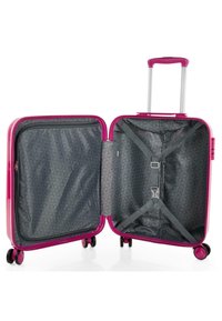 Maleta rígida rosa con un asa retráctil y cuatro ruedas. El interior cuenta con un forro gris de patrón geométrico y correas ajustables.