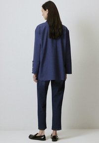 Navy striped oversized shirt with wide sleeves, buttoned cuffs, paired with dark blue denim pants and flat black shoes.