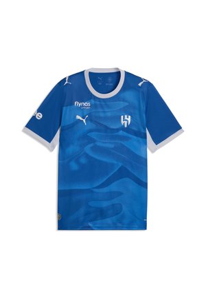 Blaues Sporttrikot mit weißen Bündchen, Puma-Logo, Sponsorenname "flynas," und weißem Schild-Emblem auf der Brust.