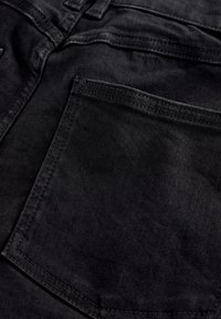 Primo piano di tessuto denim nero che mostra una tasca posteriore con cuciture e cuciture visibili.