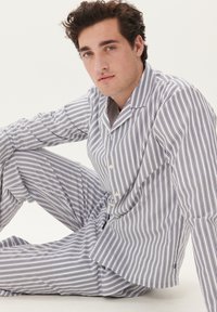 Conjunto de pijama de algodón a rayas en blanco y navy. Presenta un cierre de botones al frente, mangas largas y un corte holgado. Textura suave y diseño cómodo.