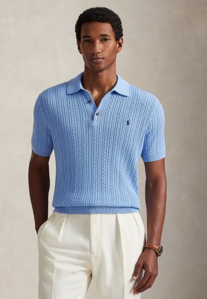 Hellblaues, gestricktes Poloshirt mit strukturiertem Zopfmuster, kurzen Ärmeln und einem weichen Kragen, kombiniert mit cremefarbenen Hosen.