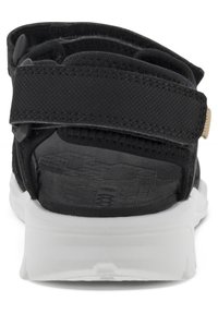 Svart sandal med justerbara remmar, med en texturerad sula och vit gummisula. Bakifrån framhävs en nätöppning och sömnadsdetaljer.