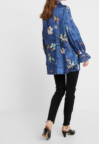 Camisa floral azul de manga larga, con un cuello volante, combinada con unos vaqueros negros ajustados y unas mules negras de tacón.