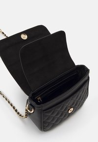 Černá prošívaná kabelka z kůže, vybavená zlatým zapínáním na cvok, řetízkovým popruhem a prázdným interiérem vyloženým semišem s přihrádkami.