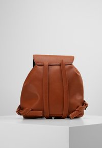 Zaino in pelle marrone con una finitura testurizzata, chiusura a rotolo e due spallacci regolabili. Presenta linee pulite e un design minimalista.