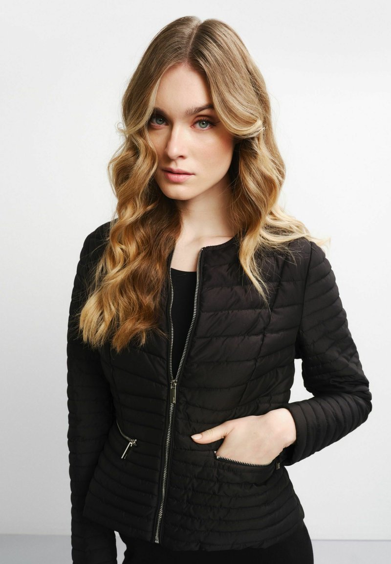 Schwarze gepolsterte Jacke mit Reißverschluss, gerippten Bündchen und Seitentaschen. Glatte Textur mit gestepptem Muster für zusätzliche Isolierung.