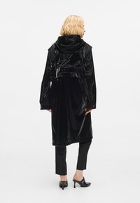 Melnas spīdīgas garas mētelis ar kapuci un īsu dizainu, ar firmas parakstu aizmugurē un slāņotu tekstūru. Kombinēts ar pielāgotām biksēm un augstpapēžu kurpēm.