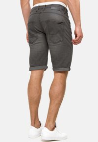 Shorts de mezclilla gris, con dobladillo enrollado, diseño de cinco bolsillos, costuras visibles, herrajes metálicos y etiqueta en la cintura. Combinados con zapatillas blancas.