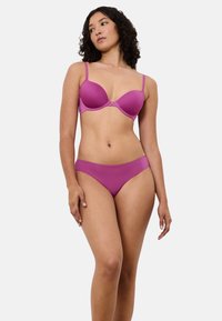 Lyserød bh med glatte skåle, justerbare stropper og et lille centralt dekorativt element. Matchende lyserøde trusser med sømløst design. Blødt, elastisk stof.