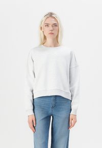 Felpa grigia chiara tagliata in morbido tessuto con colletto rotondo e spalle scese, abbinata a jeans in denim blu. Design semplice, senza motivi.