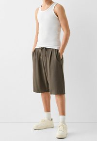 Bílý top bez rukávů a olivově zelené šortky vyrobené z měkké látky, s elastickým pasem, bočními kapsami a světle hnědými akcenty na šňůrce.