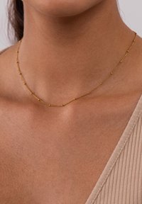 Gouden halsketting met een dunne ketting en kleine bolvormige accenten. Ontworpen om delicaat rond de nek te rusten. Gladde textuur.