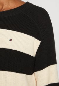 Maglione a righe nero e crema in maglia con scollatura rotonda. Presenta un tessuto testurizzato e un piccolo logo nella zona sinistra del petto.