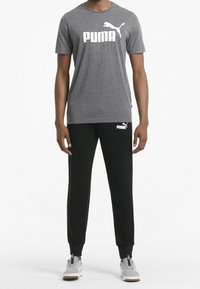 Grå t-shirt med en stor vit "PUMA" logotyp, tillsammans med svarta sweatpants som har en vit logotyp. Sneakers är grå med beige accenter.